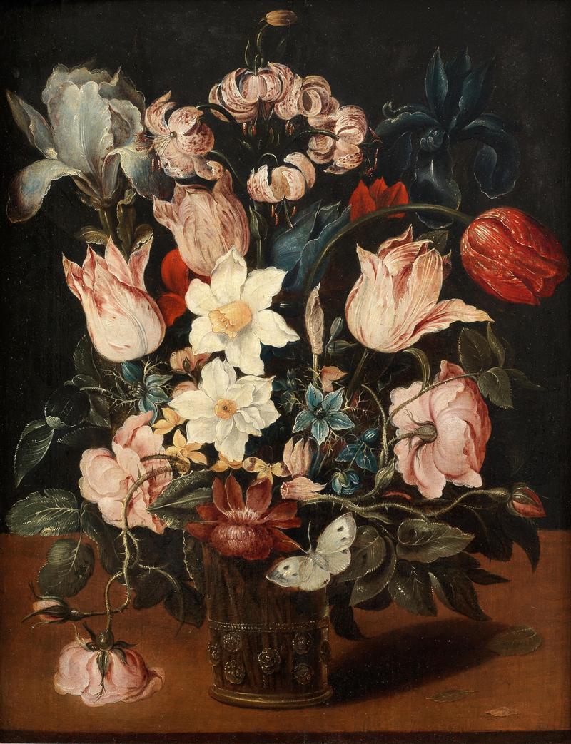 Tulips, narcissi, an iris and other flowers in a glass vase on a table top with a butterfly